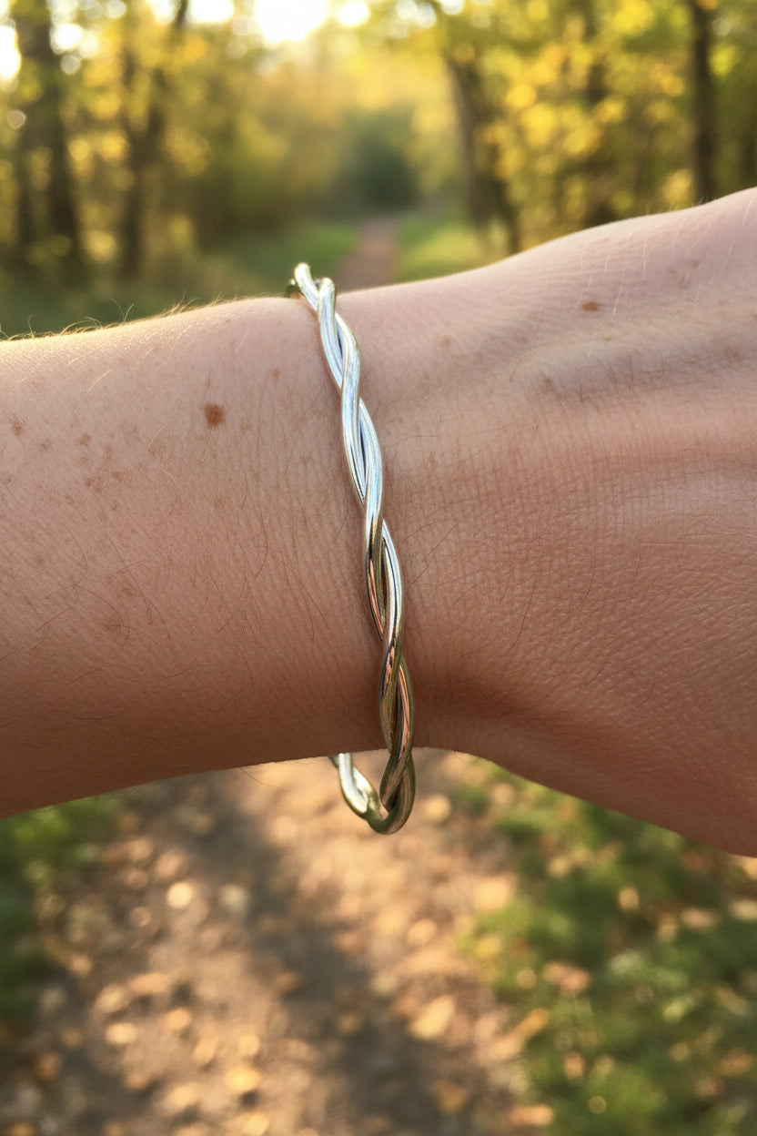 Luxe zilveren gekrulde RVS bangle armband gedragen om de pols van een vrouw in een zonnige, bosrijke natuur.