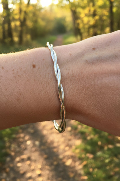 Luxe zilveren gekrulde RVS bangle armband gedragen om de pols van een vrouw in een zonnige, bosrijke natuur.