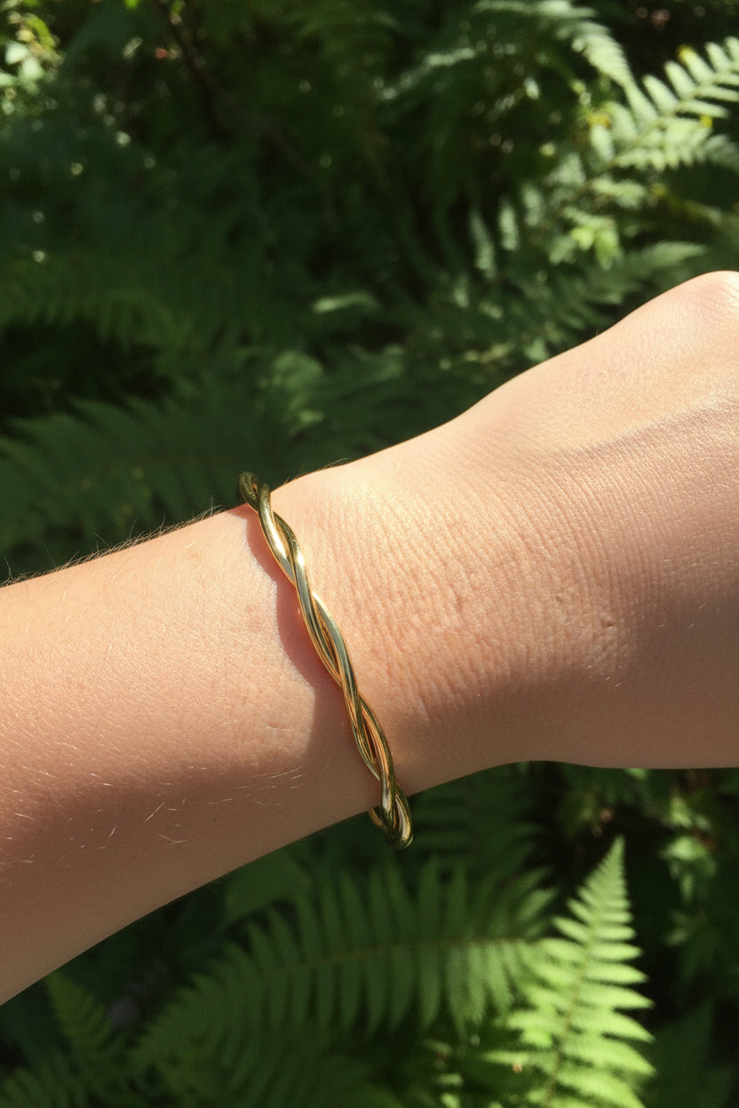 Luxe gouden gekrulde RVS bangle armband gedragen om de pols van een vrouw in een zonnige, bosrijke natuur.
