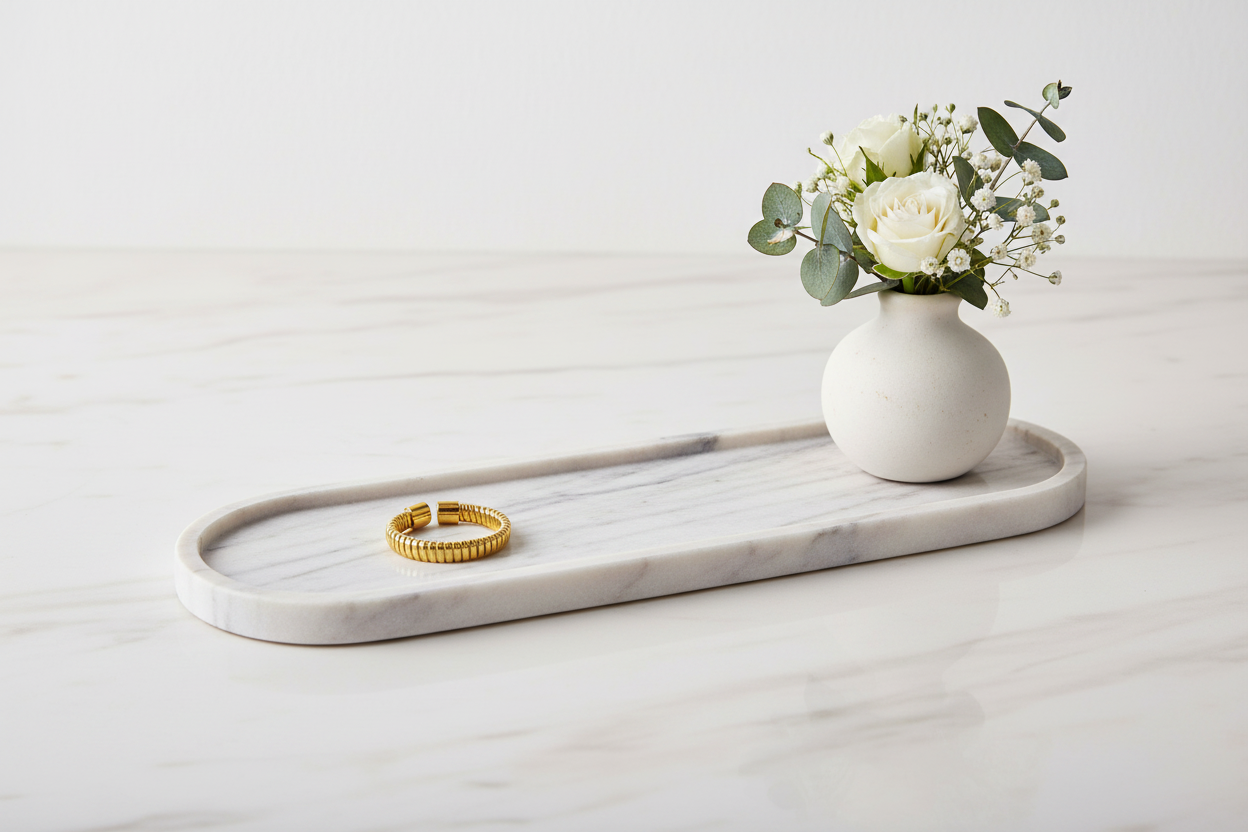 Een verstelbare gouden ring met een geribbeld design, gepresenteerd op een langwerpig wit marmeren dienblad naast een klein wit vaasje met witte rozen en eucalyptus.