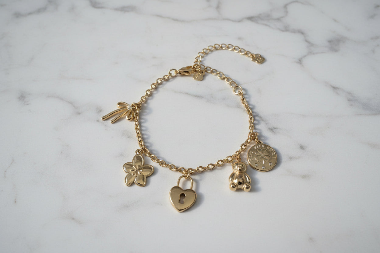 Elegante goudkleurige armband met verschillende bedels op een marmeren plaat gepresenteerd.