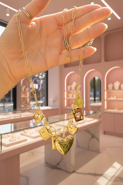 Luxe goudkleurige waterproof RVS bedelketting sfeervol vastgehouden in een hand in een luxe sieradenwinkel, met luxe vitrines en zacht roze kleur kasten met sieraden op de achtergrond..