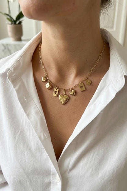 Goudkleurige RVS charmsketting met dobbelsteen-, speelkaarten- en hartbedels gedragen om de hals van een vrouw in een witte blouse.