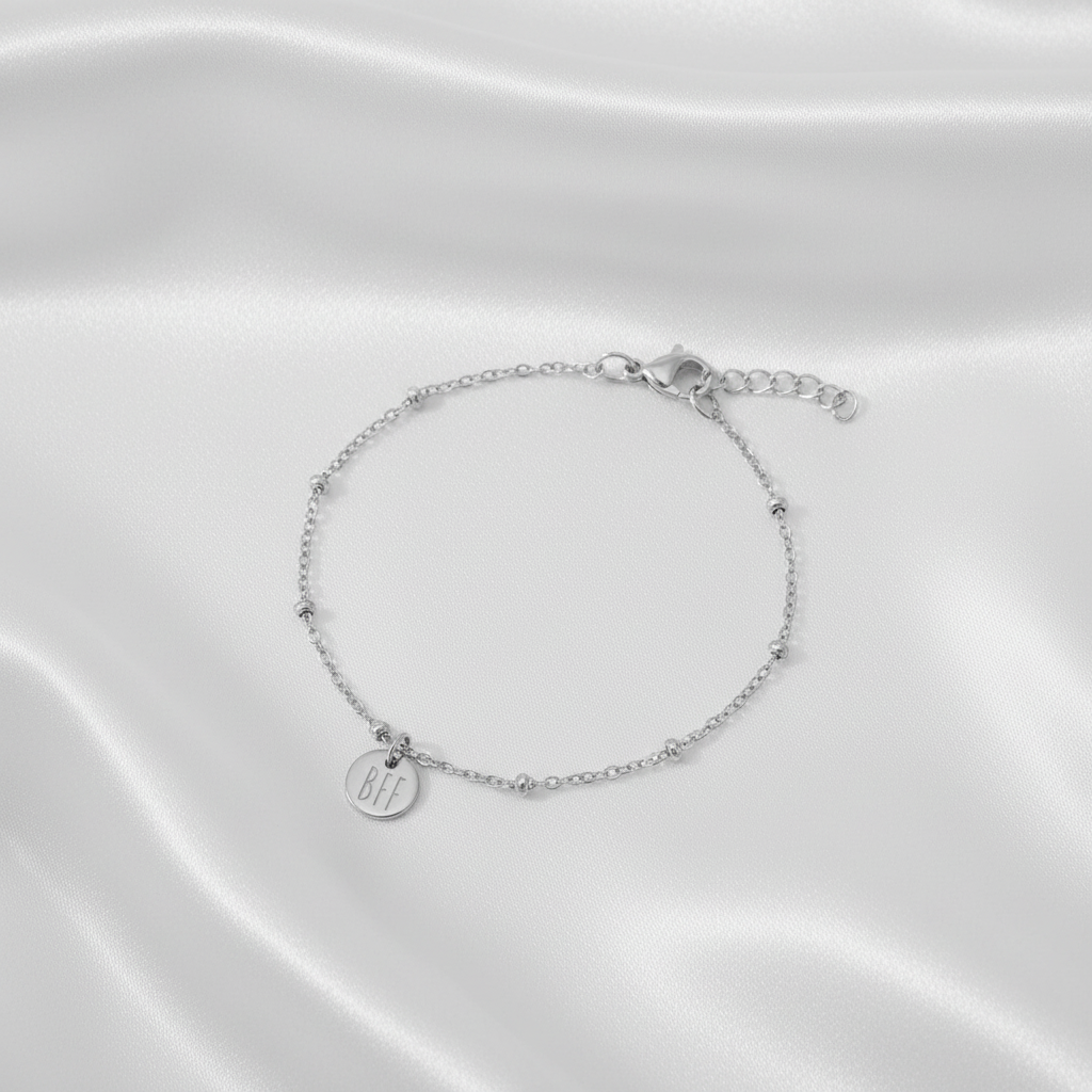 Zilveren BFF armband van stainless steel met fijne schakel en ronde bedel op witte satijnen stof, elegante en subtiele uitstraling.