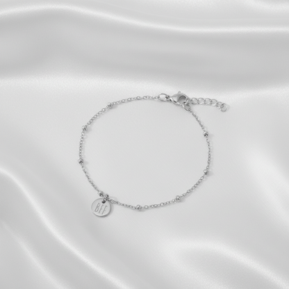 Zilveren BFF armband van stainless steel met fijne schakel en ronde bedel op witte satijnen stof, elegante en subtiele uitstraling.