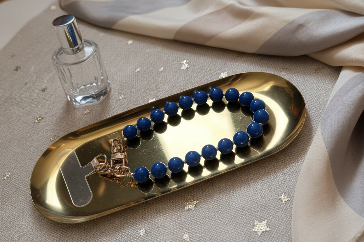 Blauwe kralen telefoonkoord met gouden details op een goudkleurige schaal en lifestyle producten eromheen.