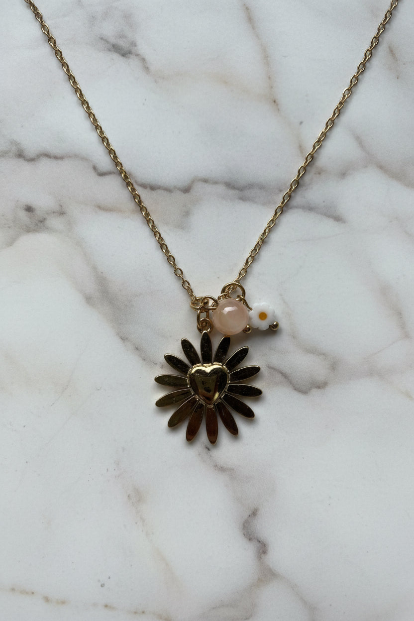 Detailopname van de gouden RVS ketting met zonnebloem hart bedel, rozenkwarts en klein wit bloemetje