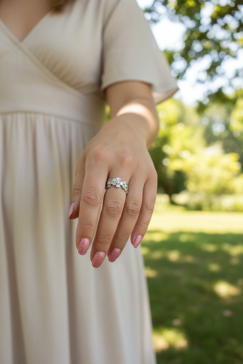 Lifestyle foto van een hand die de zilveren verstelbare madeliefjes ring draagt, gecombineerd met een elegante beige jurk in de natuur.