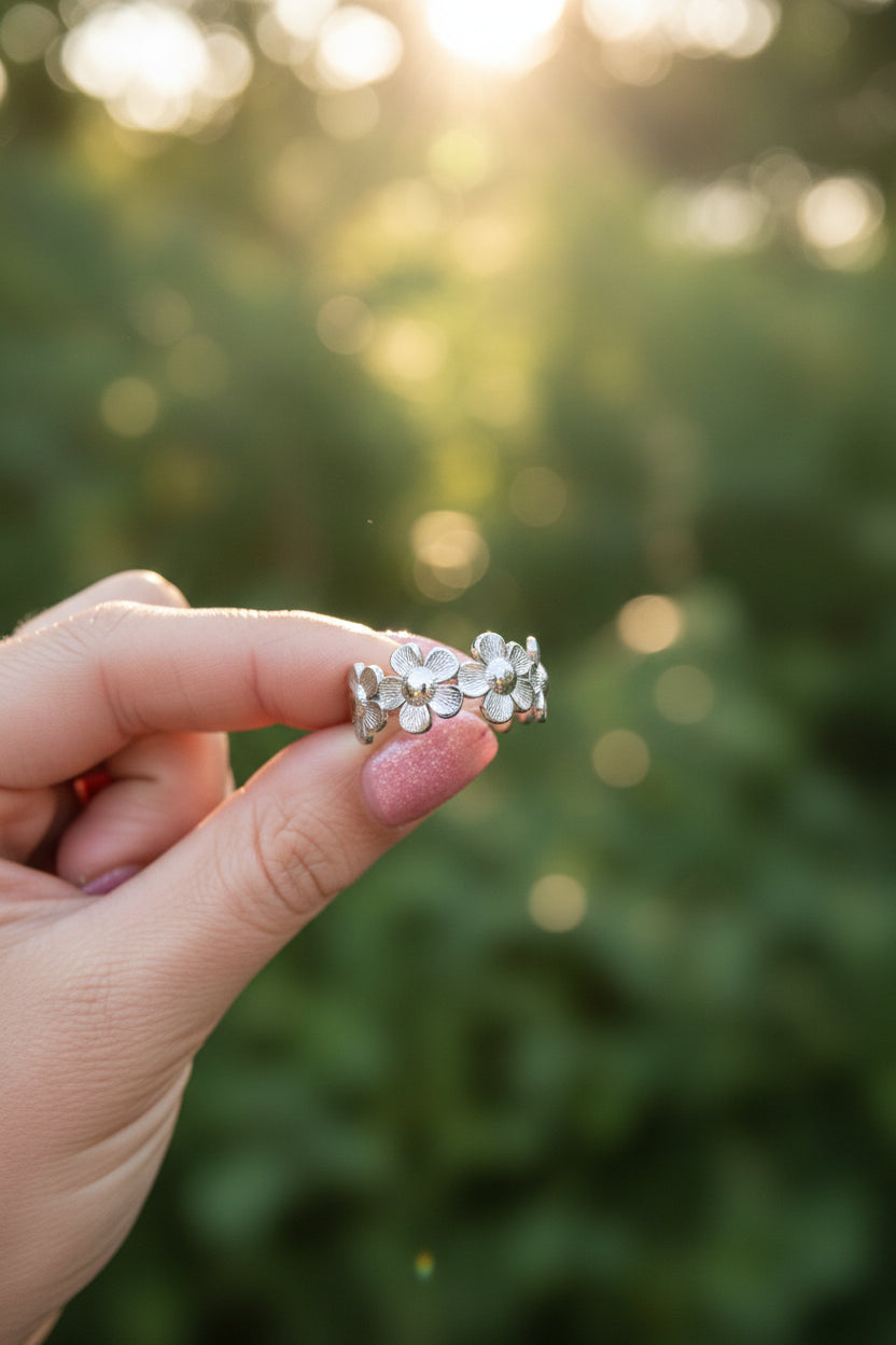 Close-up van de zilveren RVS bloemenring vastgehouden in een hand tegen een achtergrond van zomers zonlicht.
