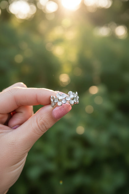 Close-up van de zilveren RVS bloemenring vastgehouden in een hand tegen een achtergrond van zomers zonlicht.