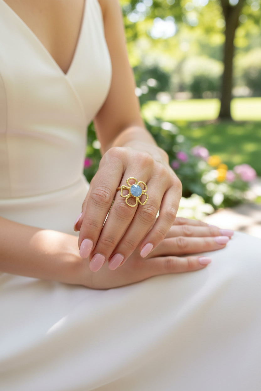 "Goudkleurige RVS bloemenring met een opvallende blauwe steen gedragen aan de hand, close-up beeld."