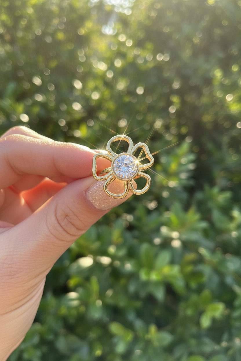 "De goudkleurige Flower ring vastgehouden in het zonlicht, waarbij de lichte steen prachtig schittert tegen een natuurlijke achtergrond."