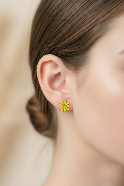 "Close-up van het rechteroor van een model met warm, blond haar dat achter haar oor is gestoken. Ze draagt één van de mini gele madeliefjes-oorknopjes van Glow Mystic in Style in haar oorlel. Het subtiele 10mm-bloemetje glinstert in natuurlijk daglicht en wordt gecombineerd met een klein, eenvoudig gouden bolletje in een tweede piercing, wat zorgt voor een moderne 'ear party'."