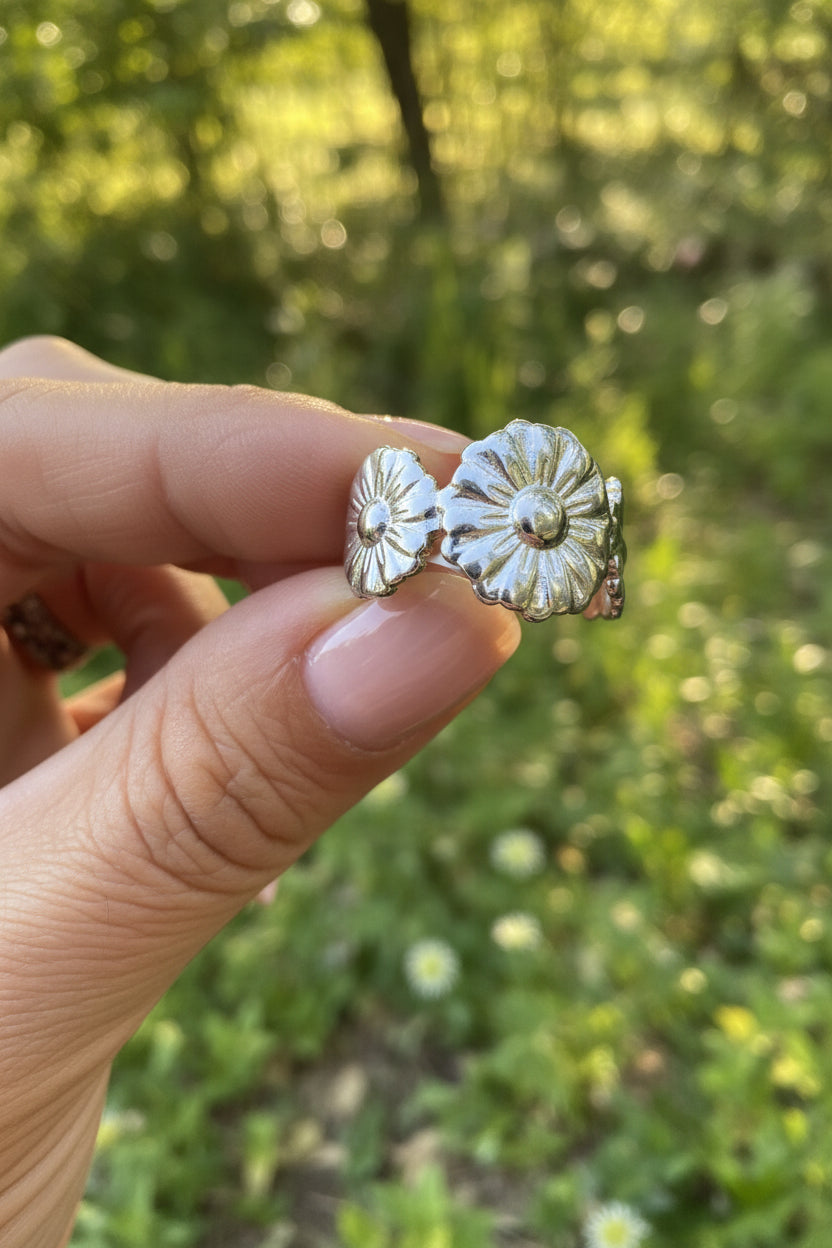 Subtiele zilveren minimalistische bloemenring van stainless steel, vastgehouden tussen de vingers in een bosrijke natuur met zachte, sfeervolle zonnestralen.