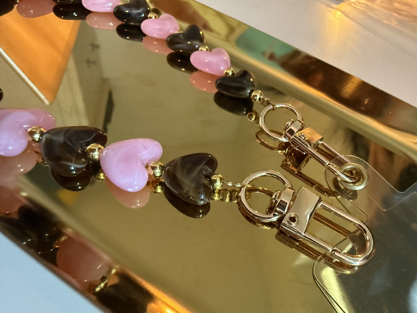 Glow Mystic in Style Close up van een bruin & roze hartjes telefoonkoord op een goudkleurige schaal.