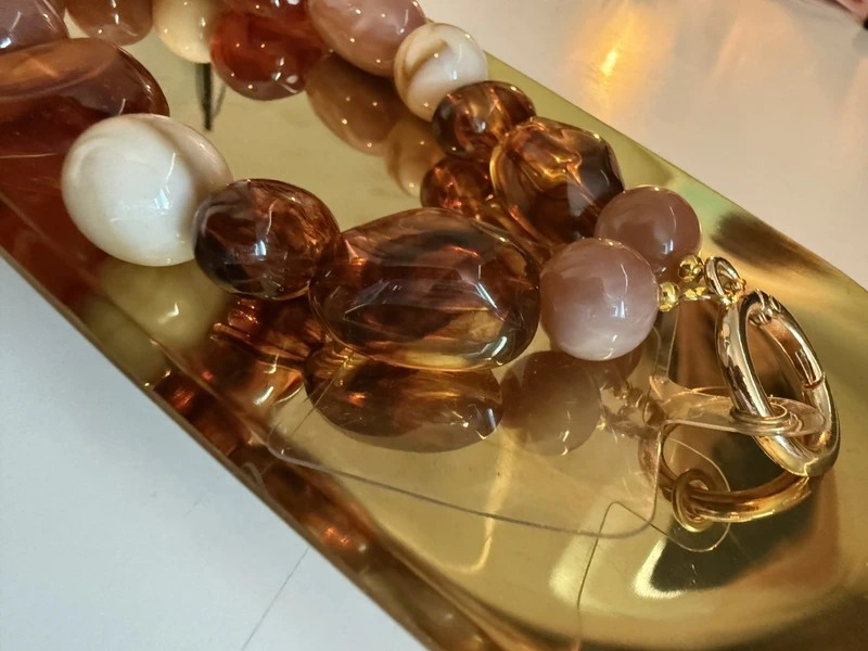 Glow Mystic in Style Close up van een telefoonkoord met grote bruine en beige kralen op een goudkleurig schaaltje.