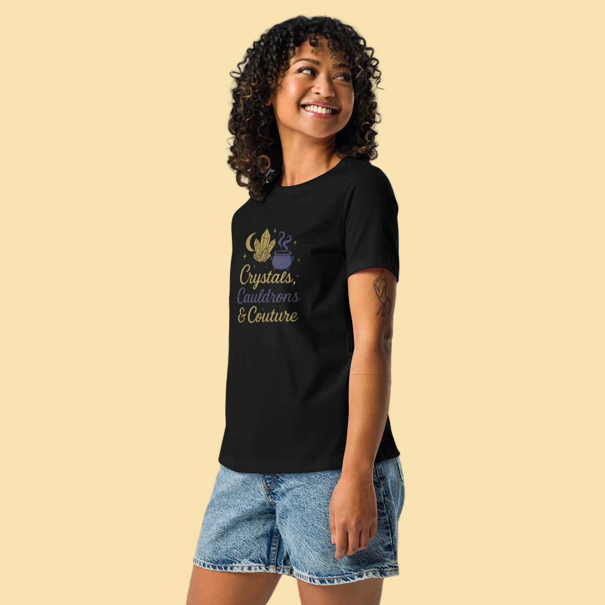 Woman wearing black Crystals Cauldrons and Couture T Shirt with gold and purple design at outdoor event
