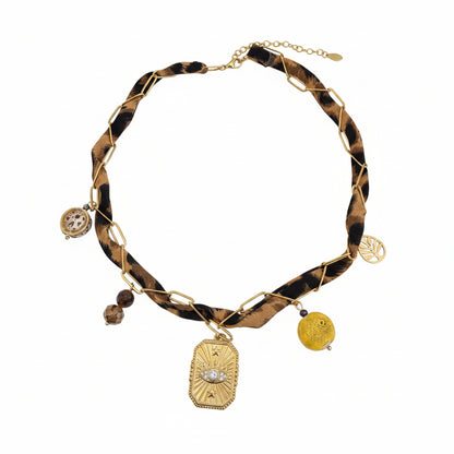 "Gedetailleerde close-up van de bedels aan de panterprint choker: een goudkleurige Evil Eye hanger, een geel keramisch kraaltje, een klein goudkleurig blaadje en bruine kristalsteentjes