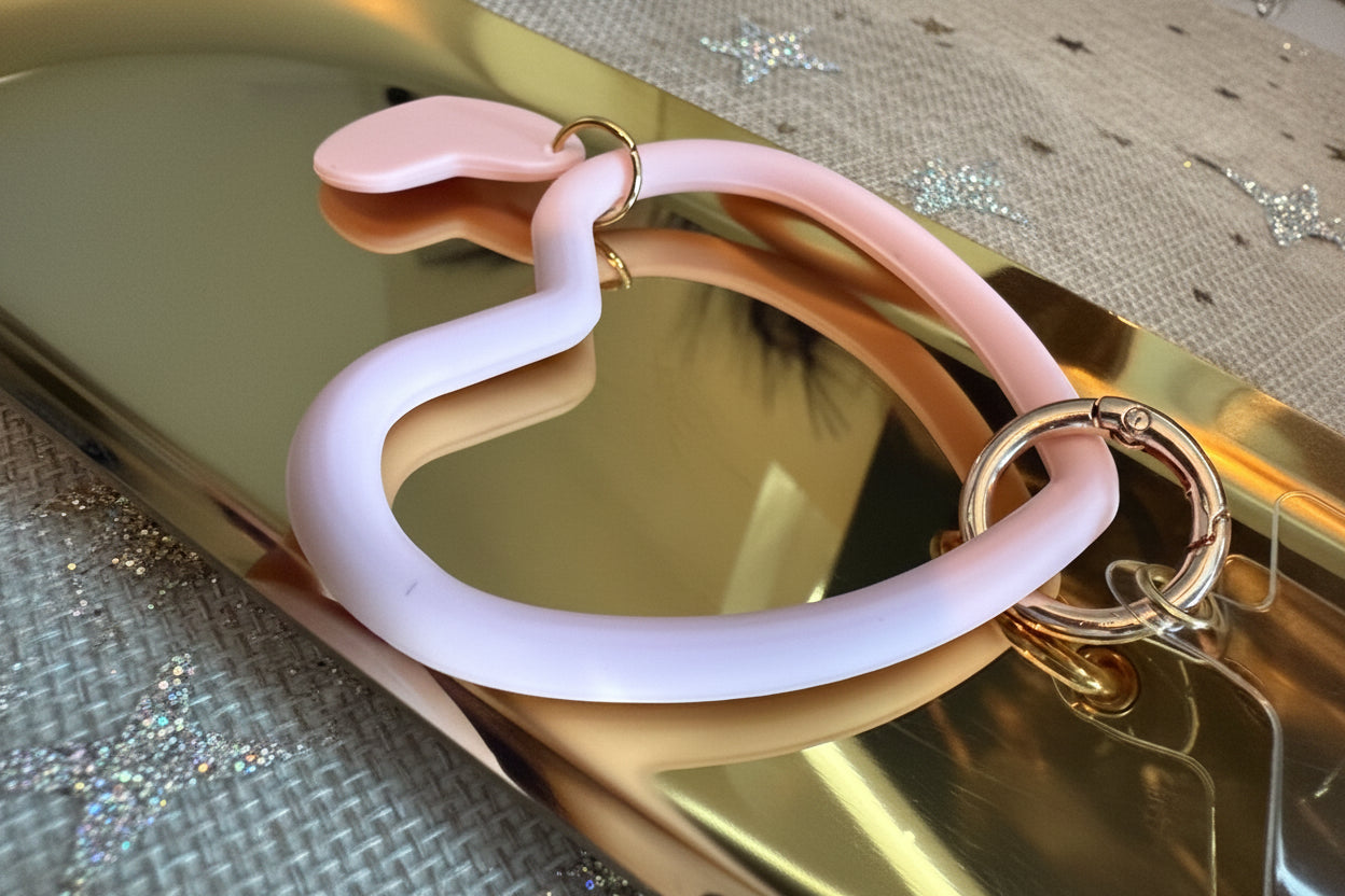 Glow Mystic in Style lichtroze siliconen hart telefoonring met gouden sluiting van dichtbij op een gouden schaal
