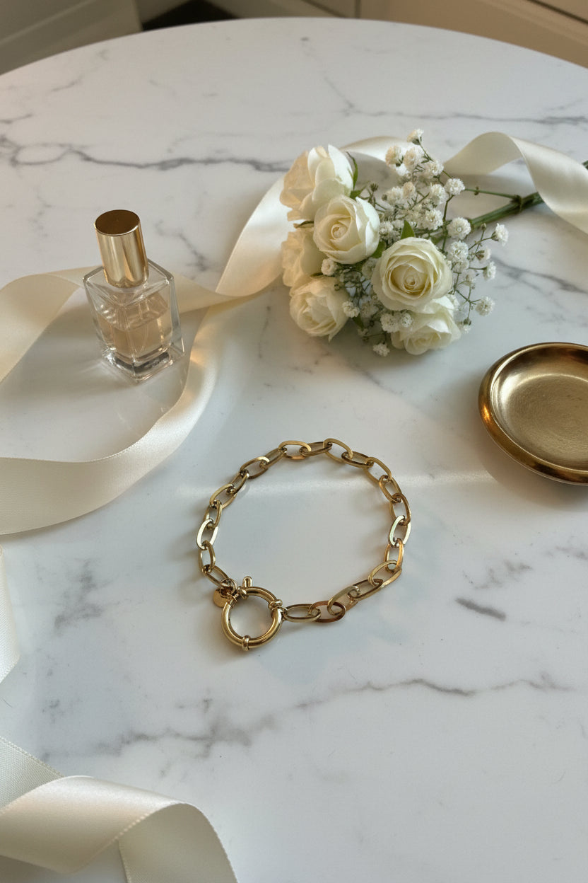 close up bedelarmband op een wit marmeren tafel met bloemen en parfum eromheen gepresenteerd