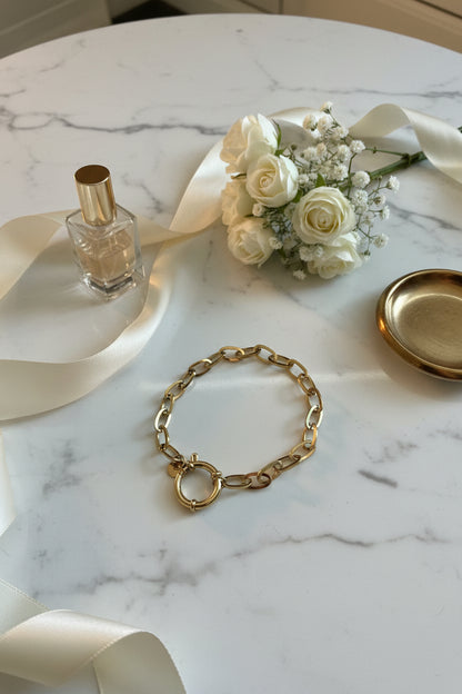 close up bedelarmband op een wit marmeren tafel met bloemen en parfum eromheen gepresenteerd