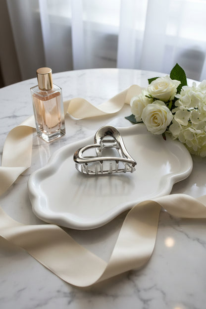 close up van een hart haarclip op een witte schaal met parfum en roosjes ernaast gepresenteerd.