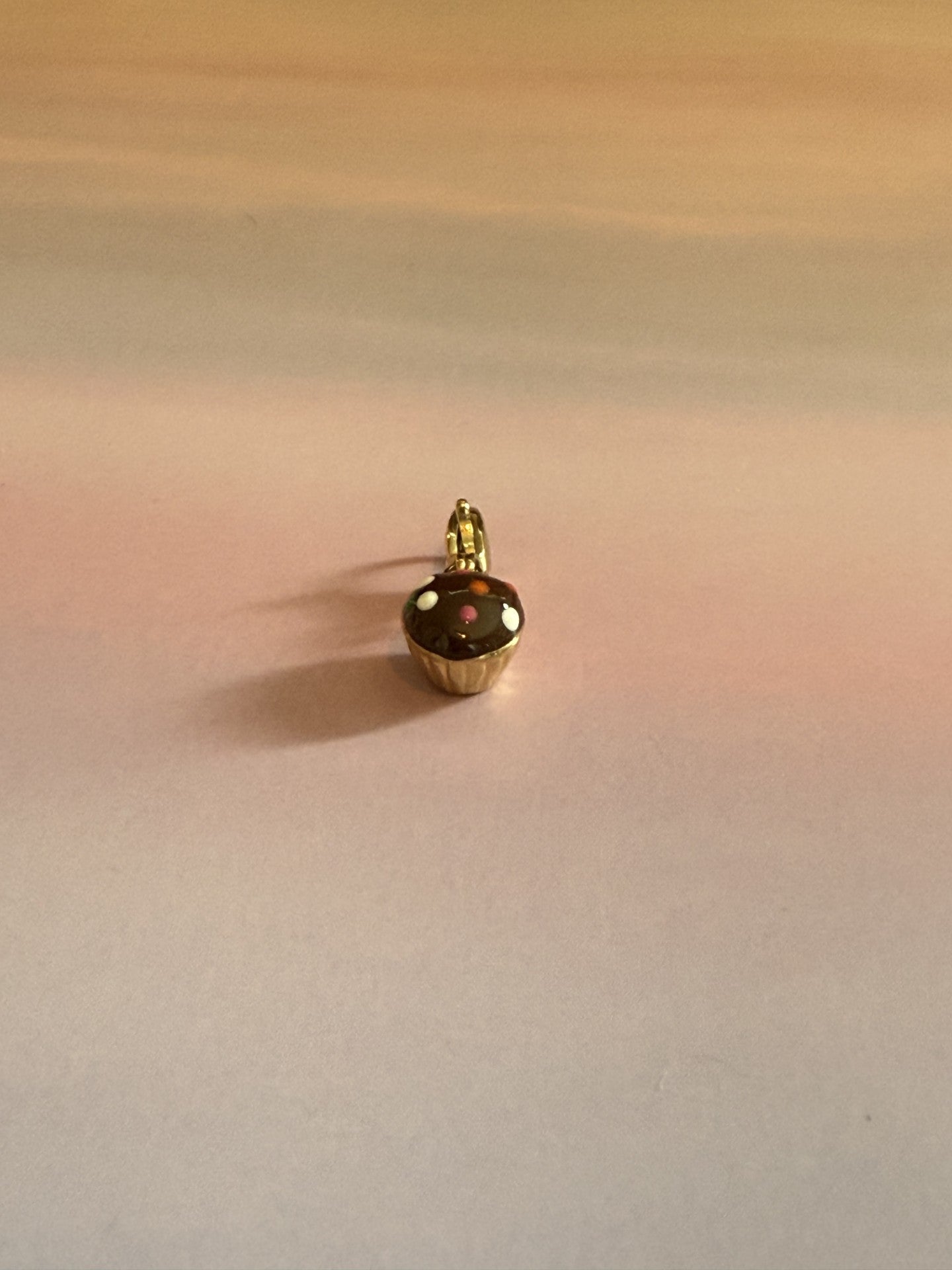 Gouden RVS cupcake bedel met emaille voor ketting of bedelarmband op gekleurde achtergrond.