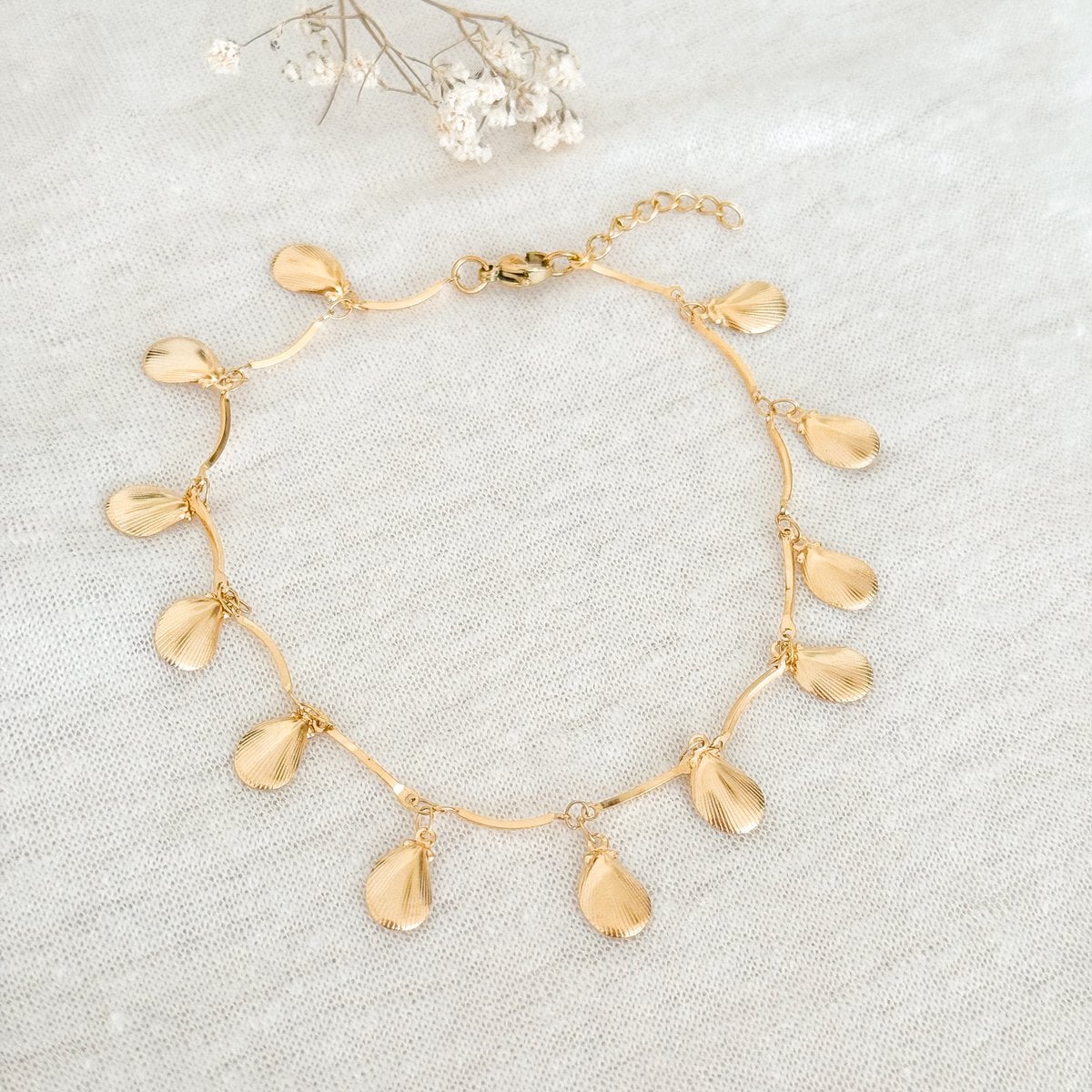 Detail van goudkleurige schelp hangertjes aan enkelbandje
