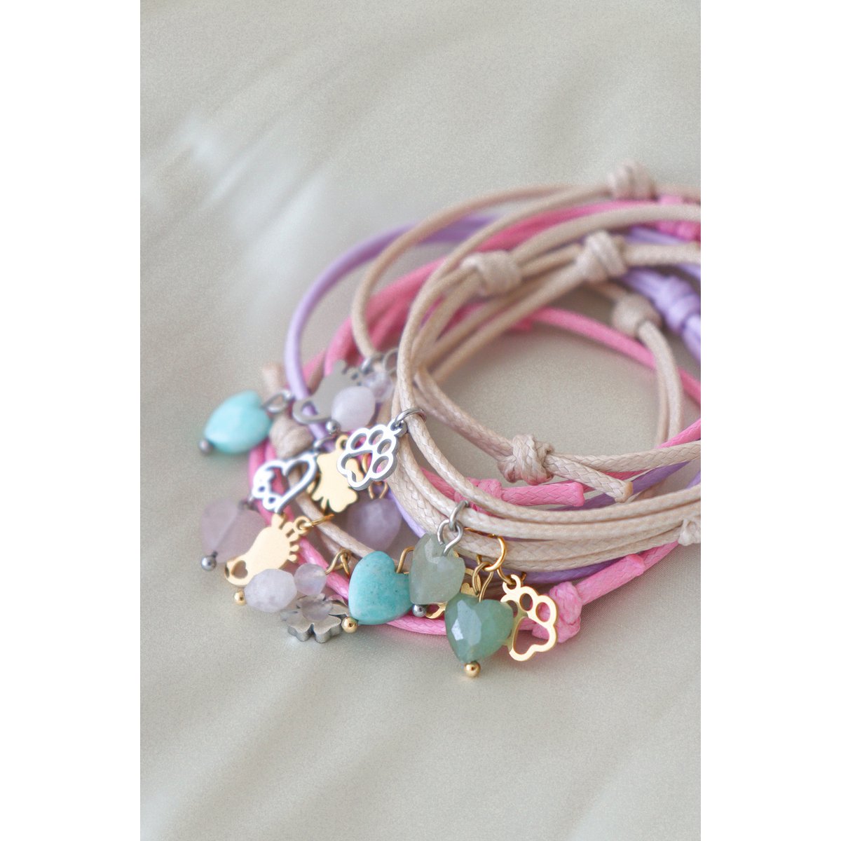 Sfeerfoto van het roze waxkoord armbandje gepresenteerd op een roze ondergrond, focus op de zachte kleur van het koord en de glanzende edelsteen."
