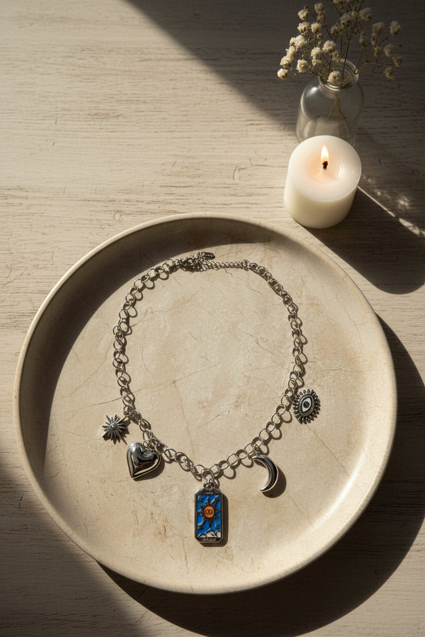Spirituele zilveren bedelketting met tarotkaart, maan en boze oog in een beige kleur schaal met een brandend kaarsje en vaasje bloemen ernaast.