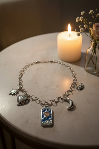Spirituele zilveren bedelketting met tarotkaart, maan en boze oog op een marmeren tafel met een kaarsje en vaasje bloemen gepresenteerd.