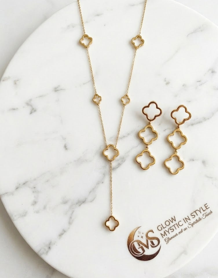 Glow Mystic in Style RVS Klaver Sieraden Set – Luxe Goud Lariat Ketting en Oorbellen op Wit Marmeren Plateau. Perfecte Upsell voor een Complete Look.