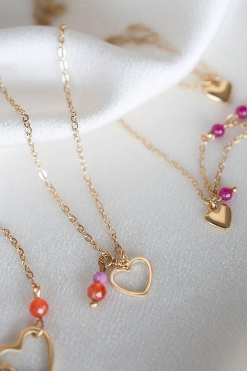 Detail van een gouden ketting met open hartje en kleurrijke edelstenen op wit satijn.