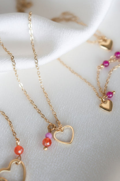 Detail van een gouden ketting met open hartje en kleurrijke edelstenen op wit satijn.