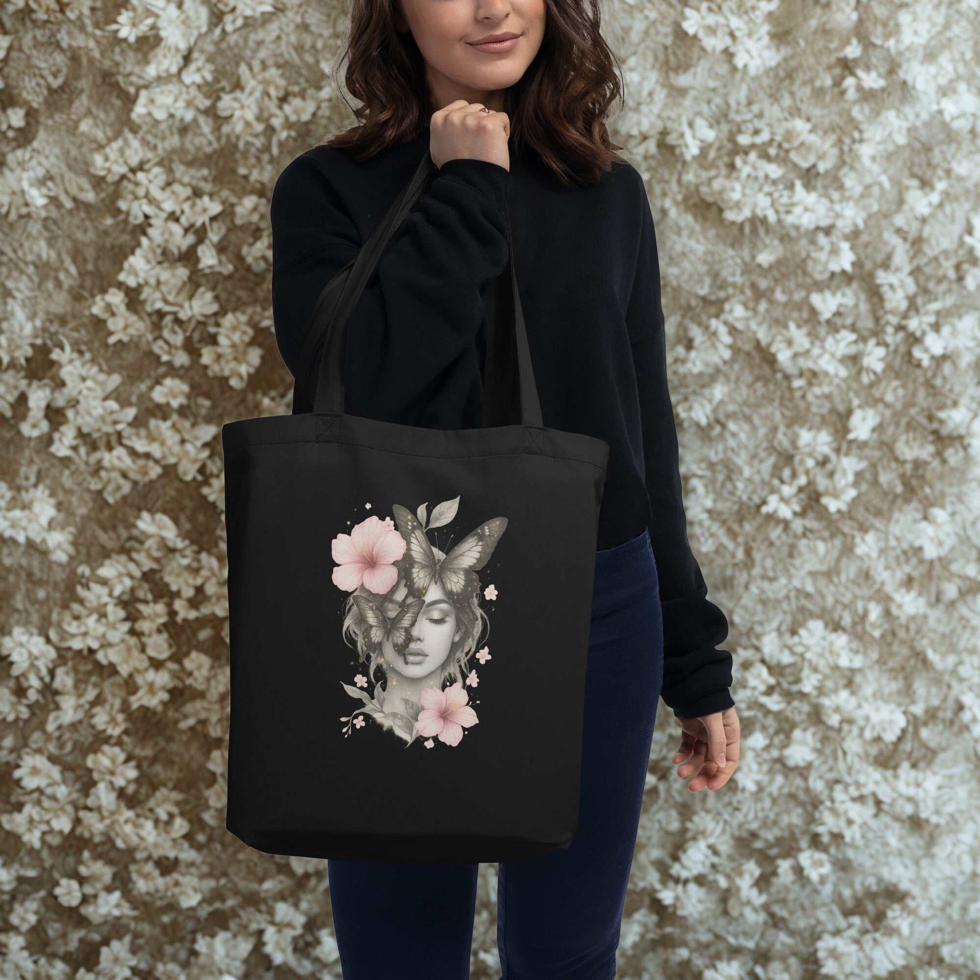 Woman holding black Eco Tote Bag with floral and butterfly design against floral background