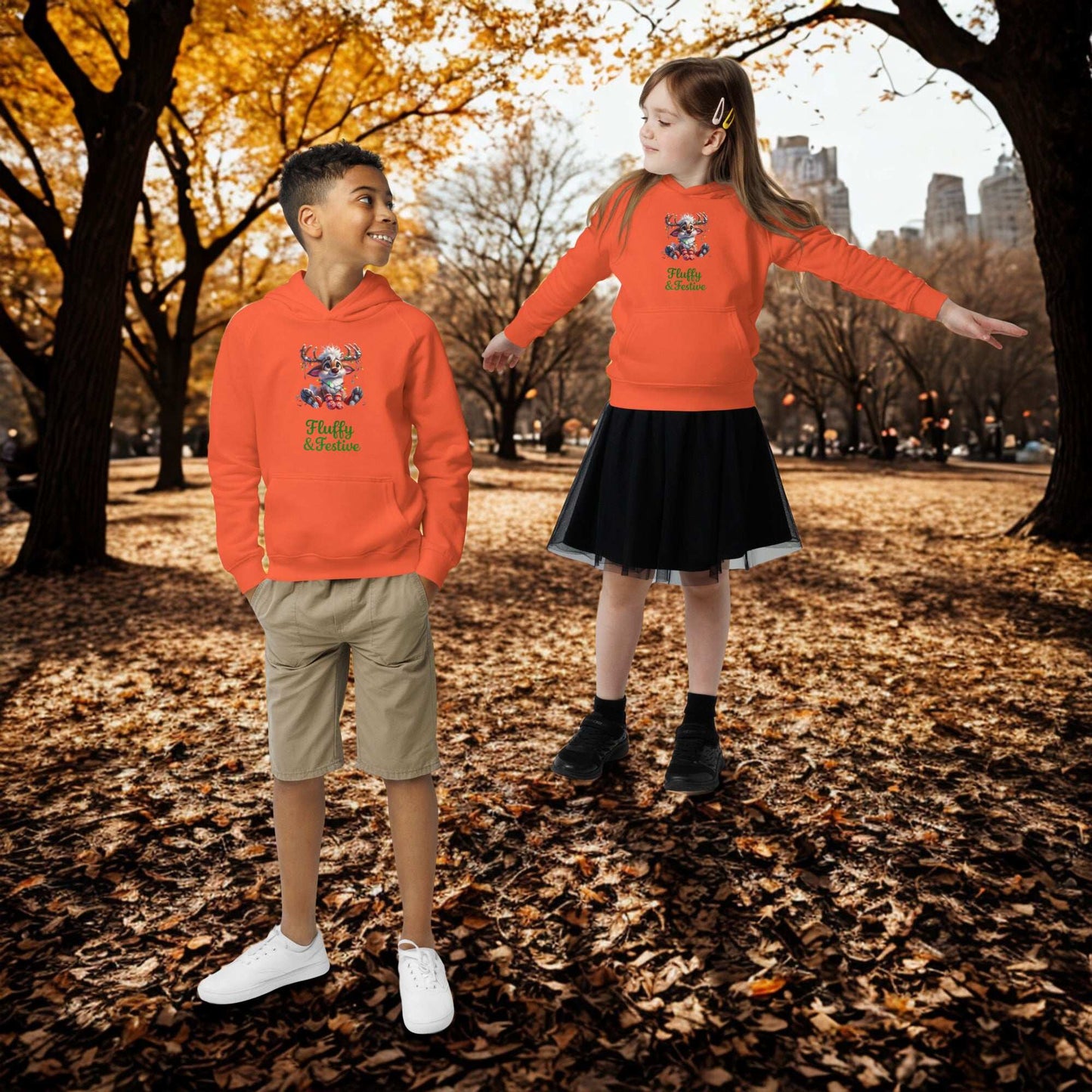 Two kids wearing bright orange Kids Christmas Hoodies outdoors in autumn with fallen leaves and trees in the background