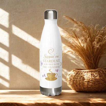 White stainless steel Sippin on Stardust Water Bottle with gold and purple design, insulated with leak-proof cap, placed on wooden surface near wicker basket.