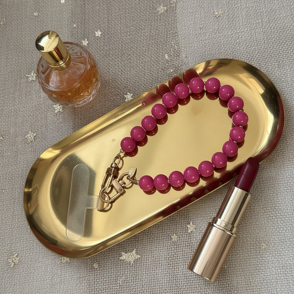Fuchsia roze kralen telefoonkoord op een goudkleurige schaal met 2 lifestyle producten eromheen.