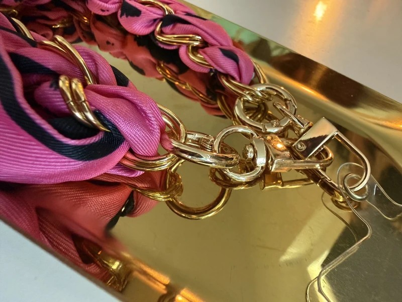 Sfeerbeeld van roze en fuchsia stoffen telefoonkoorden met goudkleurige schakels op een goudkleurige glanzende schaal.