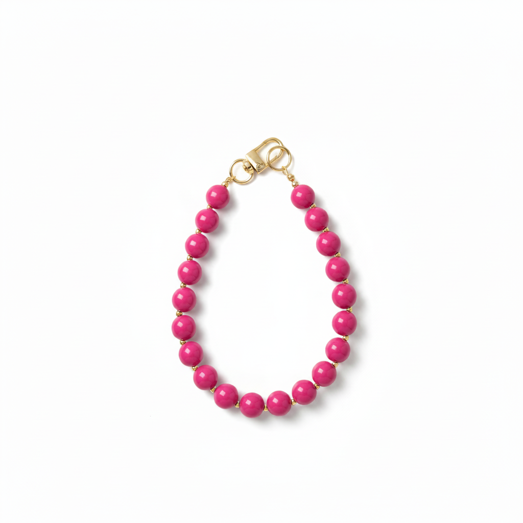 Handgemaakte fuchsia roze phone charm met gouden details op een witte achtergrond.