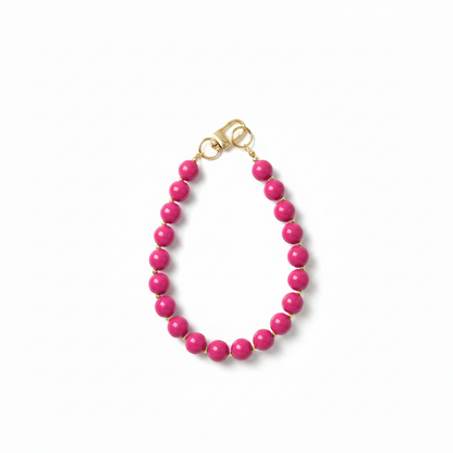 Handgemaakte fuchsia roze phone charm met gouden details op een witte achtergrond.