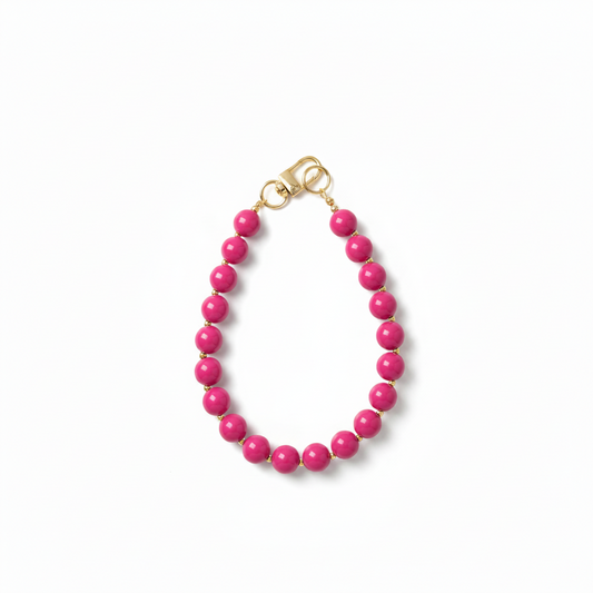 Handgemaakte fuchsia roze phone charm met gouden details op een witte achtergrond.