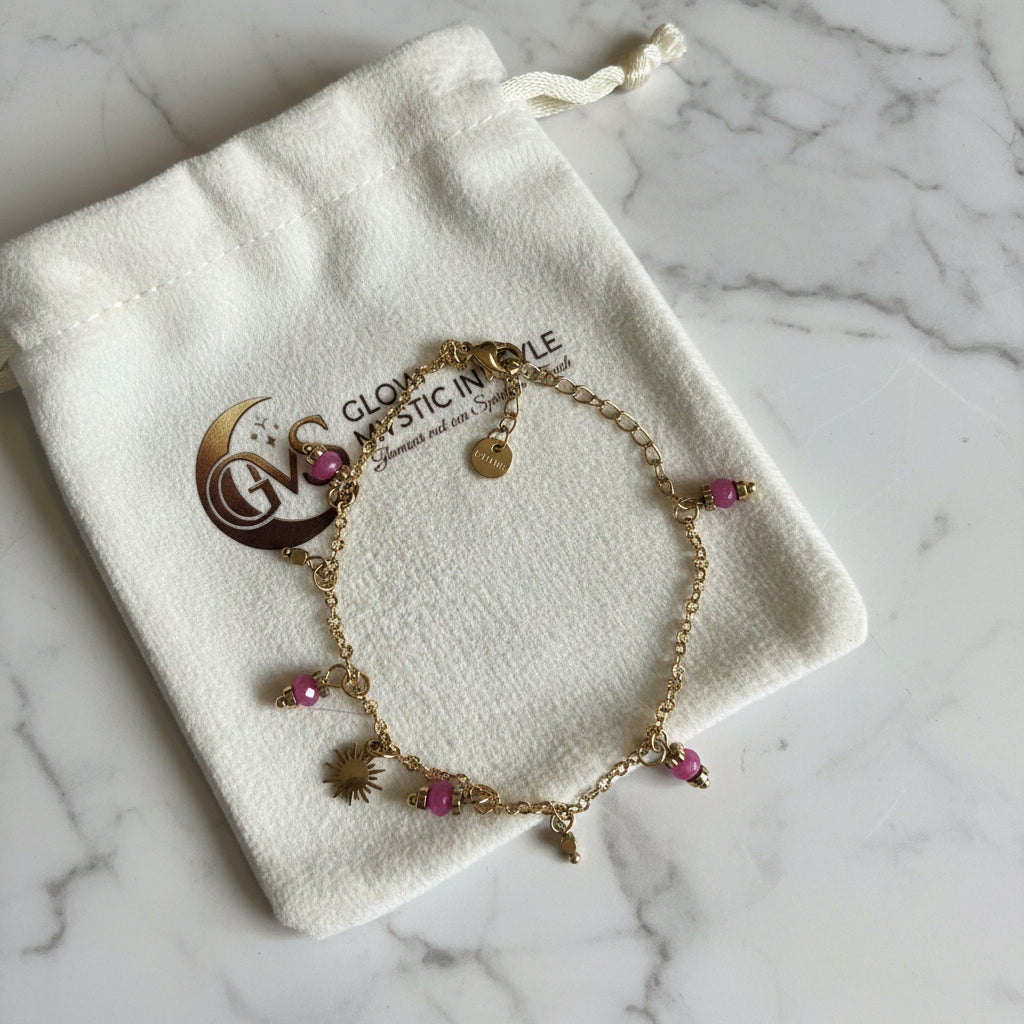 Goudkleurig rvs armbandje met zonnestralen bedeltje en fuchsia kralen op een velvet Glow Mystic in Style zakje op een heldere marmeren achtergrond.