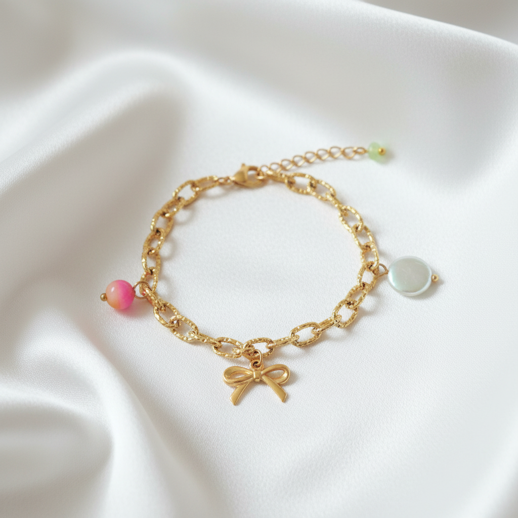 Goudkleurige statement armband met strikje, schelp en jade hanger op zachte satijnen achtergrond