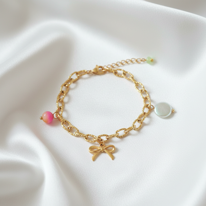 Goudkleurige statement armband met strikje, schelp en jade hanger op zachte satijnen achtergrond