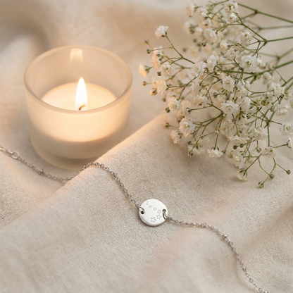 Zilverkleurige armband met sterren gravure op zachte stof met kaars en bloemen - elegant minimalistisch sieraad