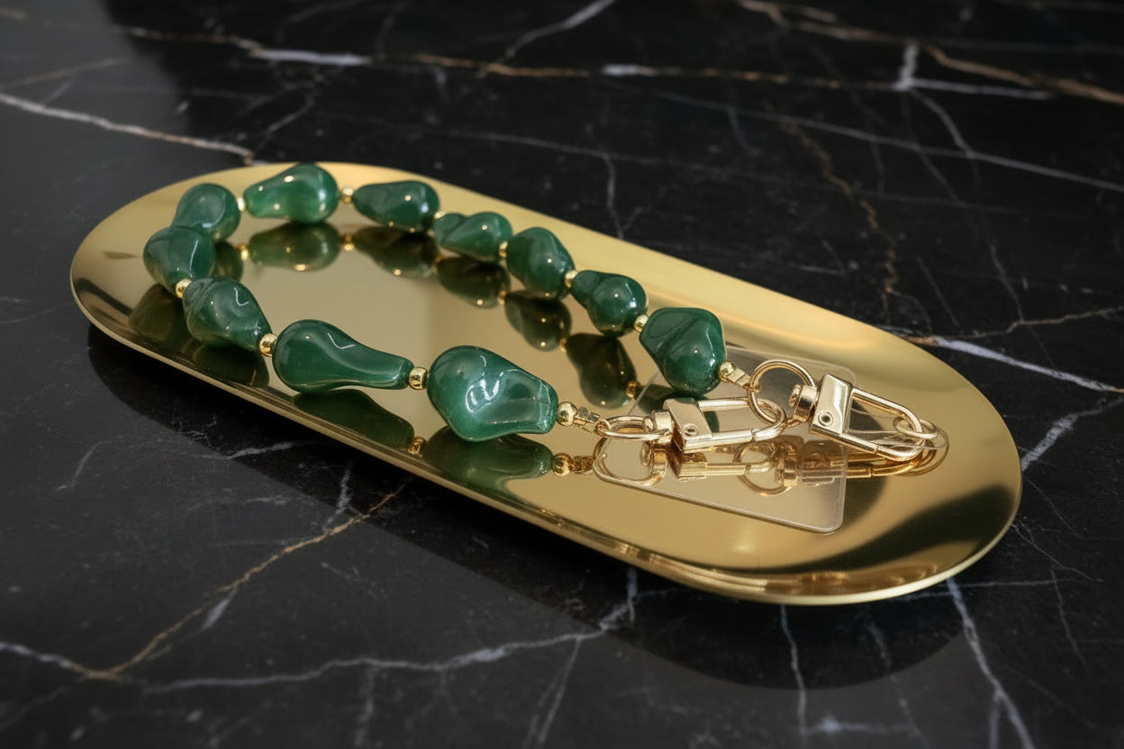 Glow Mystic in Style emerald groen acryl kralen telefoonkoord met gouden details en transparant inlegplaatje opeen gouden schaal en zwart marmeren achtergrond.