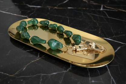 Glow Mystic in Style emerald groen acryl kralen telefoonkoord met gouden details en transparant inlegplaatje opeen gouden schaal en zwart marmeren achtergrond.