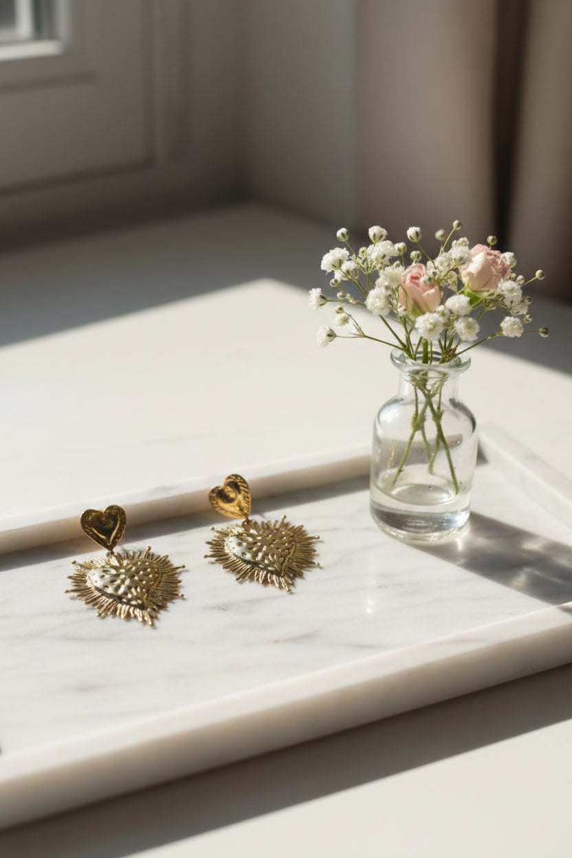 Grote gouden heilig hart statement oorbellen met stalenkrans op een marmeren tray, gestyled met een glazen vaasje gipskruid en roze droogbloemetjes.