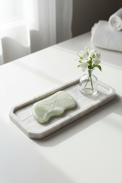 Authentieke groene Jade Gua Sha massagesteen geplaatst op een luxe marmeren plateau naast een vaas met pampaspluimen - Glow Mystic in Style.